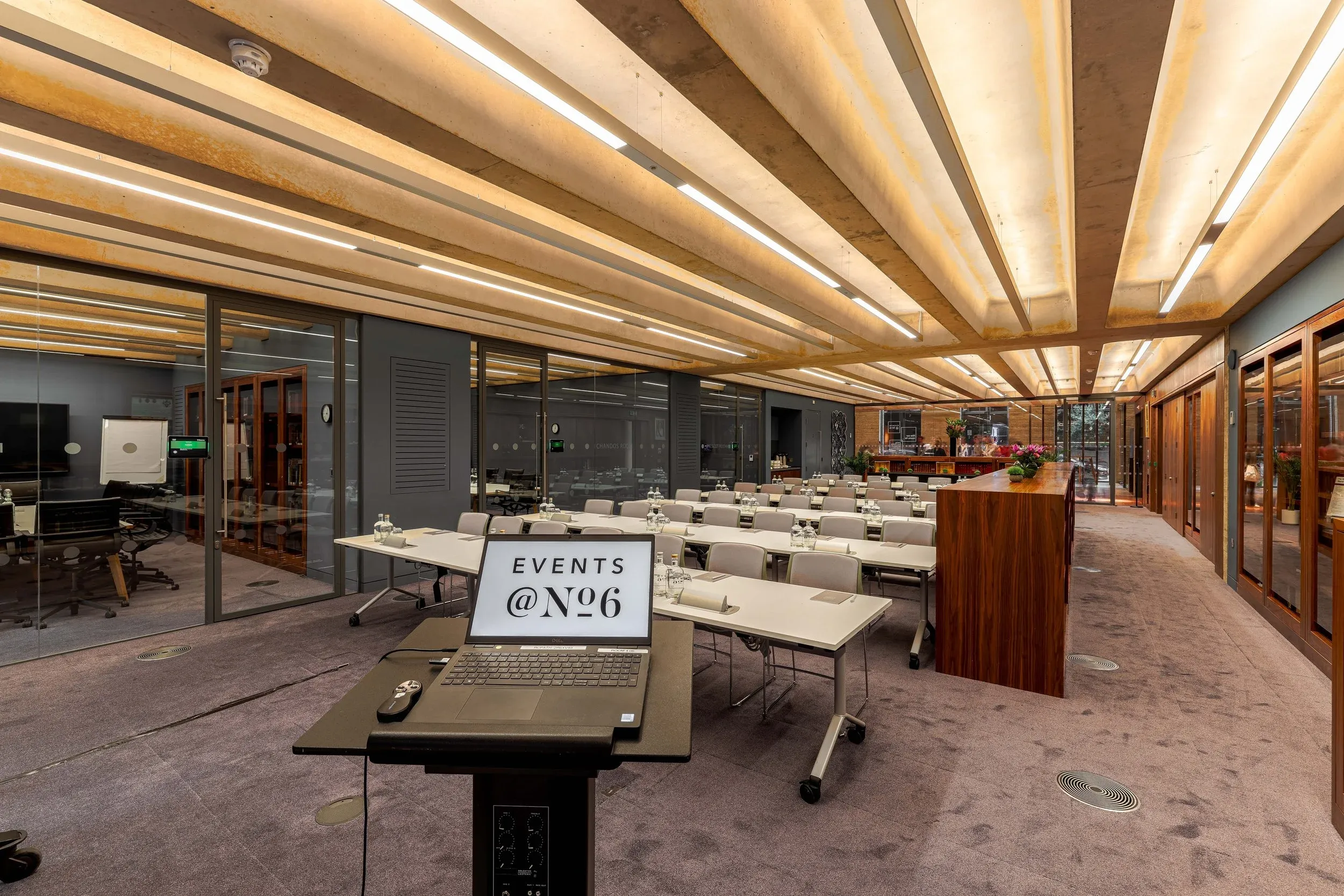 The Library set for a working session: tables in ranks facing a lectern, glass-walled breakout rooms alongside.