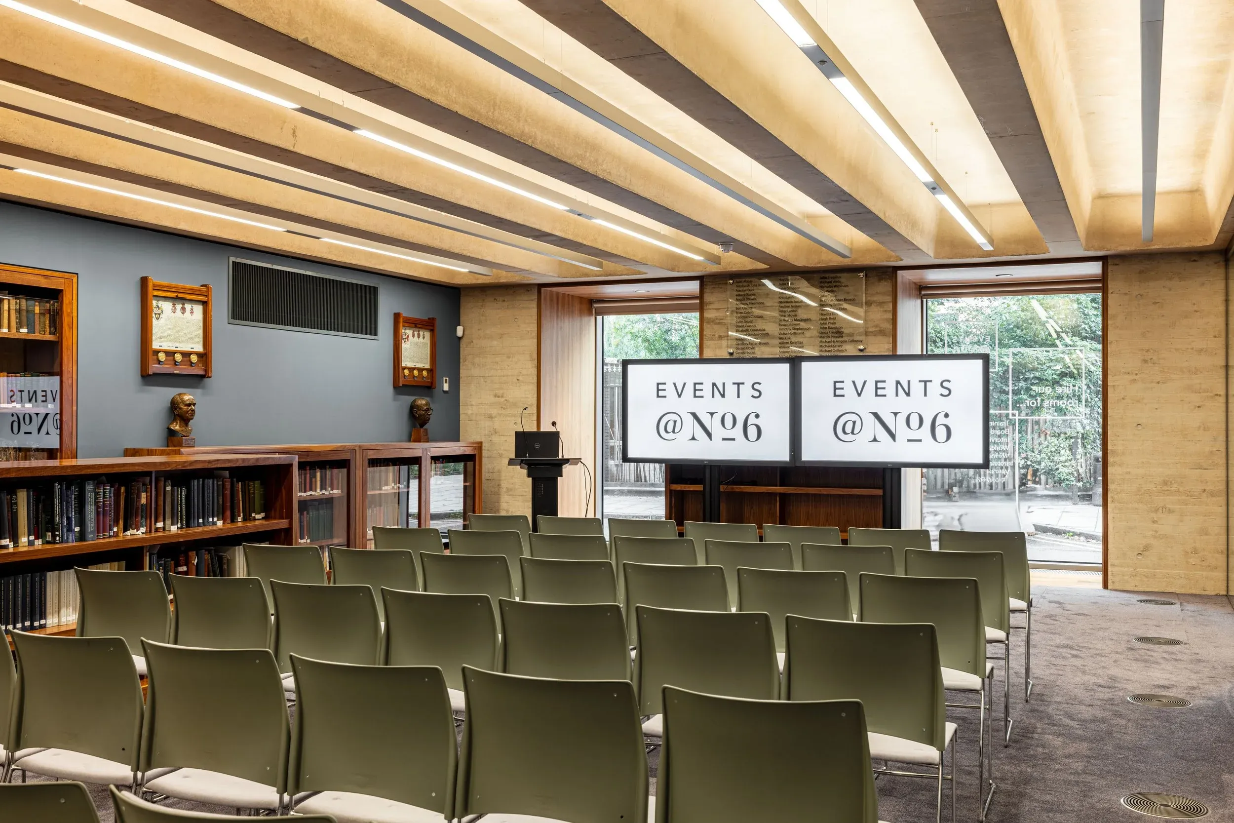 The same room in rows facing two screens, with bookcases and the garden window behind.